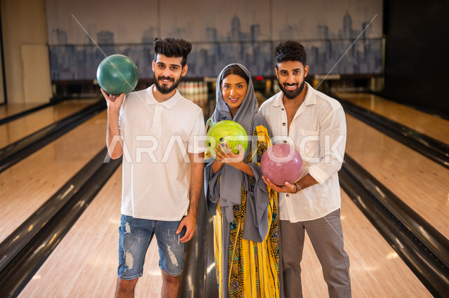 مجموعة من الاصدقاء العرب الخليجيون السعوديون يقفون بجانب بعضهم داخل ملعب البولينج ويمسكون كور البولينج، مضمار البولينج، انشطه ترفيهيه رياضية، كره البولينج الترفيهية، انشطه ورياضات شبابية، منافسات وتحديات، فريق من الاصدقاء في ملعب البولينج