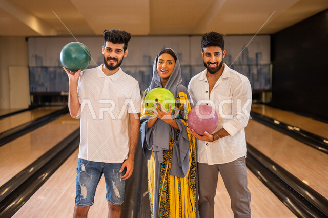 مجموعة من الاصدقاء العرب الخليجيون السعوديون يقفون بجانب بعضهم داخل ملعب البولينج ويمسكون كور البولينج، مضمار البولينج، انشطه ترفيهيه رياضية، كره البولينج الترفيهية، انشطه ورياضات شبابية، منافسات وتحديات، فريق من الاصدقاء في ملعب البولينج