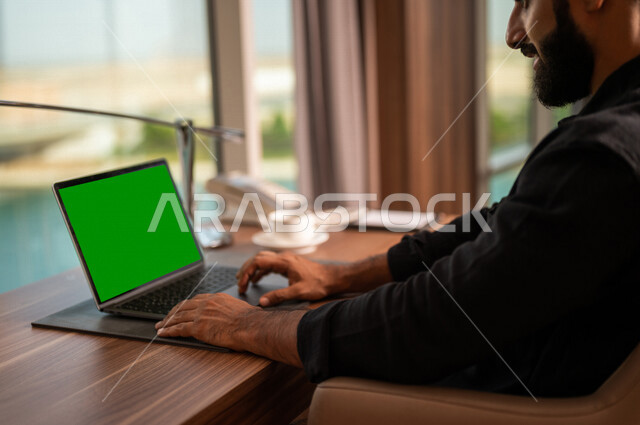 صورة مقربة لشاب عربي خليجي سعودي يستخدام حاسوب محمول بشاشة كروما خضراء، اجراء مكالمة فيديو، انجاز الاعمال و المهام، بث فيديو مباشر، دردشة وتواصل، عطلة صيفية، التعارف والتواصل الاجتماعي، صداقات عبر الانترنت، التواصل مع العملاء