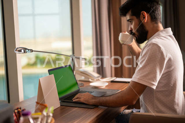 صورة مقربة لشاب عربي خليجي سعودي يستخدام حاسوب محمول بشاشة كروما خضراء، اجراء مكالمة فيديو، انجاز الاعمال و المهام، بث فيديو مباشر، دردشة وتواصل، عطلة صيفية، التعارف والتواصل الاجتماعي، صداقات عبر الانترنت، التواصل مع العملاء