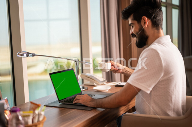 صورة مقربة لشاب عربي خليجي سعودي يستخدام حاسوب محمول بشاشة كروما خضراء، اجراء مكالمة فيديو، انجاز الاعمال و المهام، بث فيديو مباشر، دردشة وتواصل، عطلة صيفية، التعارف والتواصل الاجتماعي، صداقات عبر الانترنت، التواصل مع العملاء