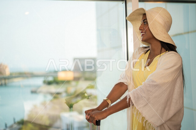 Close-up of a Saudi Arabian Gulf woman on a tourist trip, a window overlooking the waterfront in Jeddah, wearing a summer casual outfit, a travel bag, preparing for the summer vacation, a hotel resort, fun summer activities