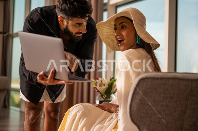 صورة مقربة لزوجان عربيان خليجيان سعوديان في رحلة شهر العسل، حجز رحلات سياحية عبر الانترنت، اكتشاف وجهات سياحية في السعودية، طلبات تسوق اونلاين، إيماءات وإشارات وجه  تدل على المفاجئة، عروض صيفية، رحلات ترفيهية لشهر العسل، خدمات فندقية سياحية 