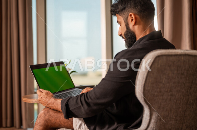 صورة مقربة لشاب عربي خليجي سعودي يستخدام حاسوب محمول بشاشة كروما خضراء، اجراء مكالمة فيديو، انجاز الاعمال و المهام، بث فيديو مباشر، دردشة وتواصل، عطلة صيفية، التعارف والتواصل الاجتماعي، صداقات عبر الانترنت، التواصل مع العملاء