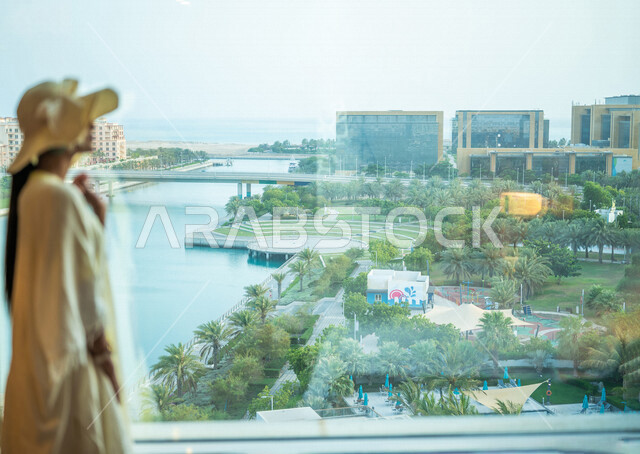 امرأة عربية خليجية سعودية ترتدي زي صيفي وتقف امام شرفة غرفة فندقية، المتعة والاستجمام، اطلالة على الواجهه البحرية في جدة، إشراقة يوم جديد، رؤية مستقبلية، قضاء اوقات ممتعة، مكان اقامة، بيت للعطلة الصيفية، وجهات السياحة في السعودية