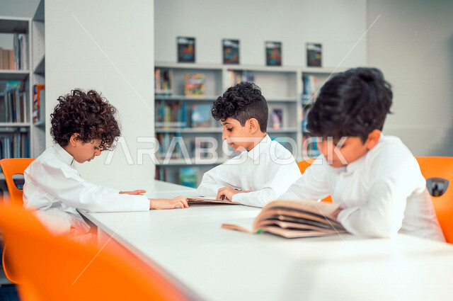 طلاب عرب سعوديون خليجيون يجلسون في المكتبة المدرسية، الاستمتاع بقراءة الكتب، مفهوم التعليم الذاتي, مكتبة المدرسة، بيئه مدرسيه تعليميه متطوره, المدارس المبتكره, جودة التعليم, مدارس أكاديميه في المملكة العربية السعودية