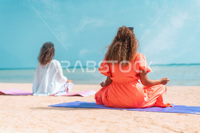 صورة من الخلف لشابتان عربيتان خليجيتان سعوديتان تمارسان رياضة اليوغا التأملية على شاطيء بحر جدة، ممارسة نشاط رياضي، أنشطة و تمارين رياضية، التأمل والاسترخاء، الرياضة والنشاط البدني، تمارين اللياقة البدنية، أسلوب حياة صحي، لياقة ورشاقة