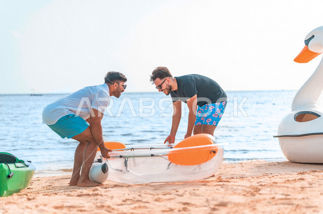 صديقان عربيان خليجيان سعوديان يرتدون النظارة الشمسية ويقضيان وقت ممتع سويا على بحر جدة السياحي، قارب التجديف البلاستيكي الشفاف، الاستعداد لركوب زورق التجديف، أنشطة ترفيهية شبابية، المتعة بين الأصدقاء، هوايات ورياضات شبابية، سياحة وإستجمام، العطلة الصيفية