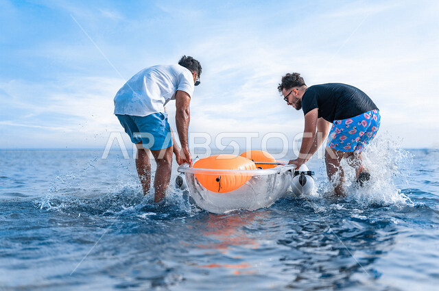 صديقان عربيان خليجيان سعوديان يرتدون النظارة الشمسية ويقضيان وقت ممتع سويا على بحر جدة السياحي، قارب التجديف البلاستيكي الشفاف، الاستعداد لركوب زورق التجديف، أنشطة ترفيهية شبابية، المتعة بين الأصدقاء، هوايات ورياضات شبابية، سياحة وإستجمام، العطلة الصيفية