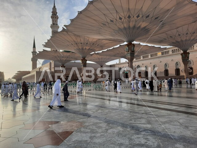 ساحة المسجد النبوي الشريف في المدينة المنورة بالمملكة العربية السعودية، العبادة والتقرب الى الله، الحرم النبوي الشريف، أماكن إسلامية مقدسة، المسلمون يمشون في المجمع الخارجي للمسجد النبوي في المدينة المنورة، المظلات الإلكترونية