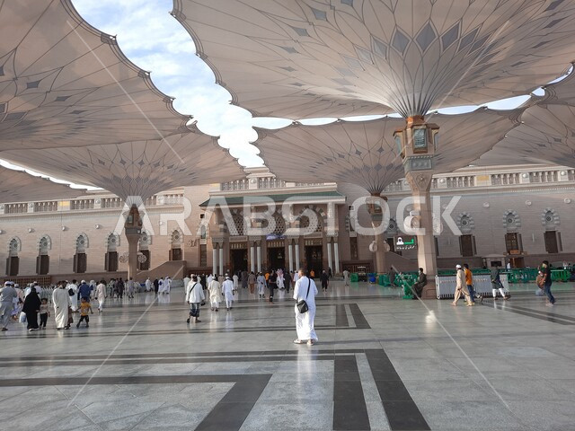ساحة المسجد النبوي الشريف في المدينة المنورة بالمملكة العربية السعودية، العبادة والتقرب الى الله، الحرم النبوي الشريف، أماكن إسلامية مقدسة، المسلمون يمشون في المجمع الخارجي للمسجد النبوي في المدينة المنورة، المظلات الإلكترونية