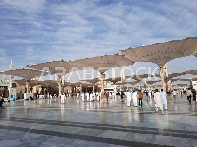 ساحة المسجد النبوي الشريف في المدينة المنورة بالمملكة العربية السعودية، العبادة والتقرب الى الله، الحرم النبوي الشريف، أماكن إسلامية مقدسة، المسلمون يمشون في المجمع الخارجي للمسجد النبوي في المدينة المنورة، المظلات الإلكترونية