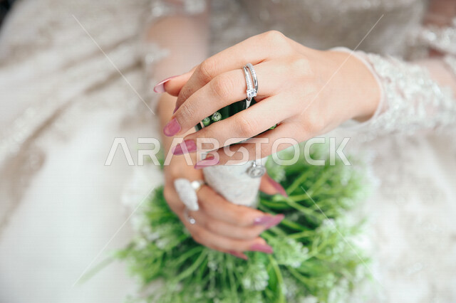 صورة مقربة عروسة ترتدي بدلة الزفاف البيضاء وتحمل بيدها باقة ورد جميلة، عروسة ترتدي خاتم الزفاف، اطلالة جميلة لعروسة يوم زفافها، ليلة العمر، مناسبات وأفراح