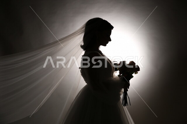 صورة ظلية لعروسة ترتدي بدلة الزفاف البيضاء وتحمل بيدها باقة ورد جميلة، اطلالة جميلة لعروسة يوم زفافها، ليلة العمر، عروسة بالمسكة والطرحة، مناسبات وأفراح