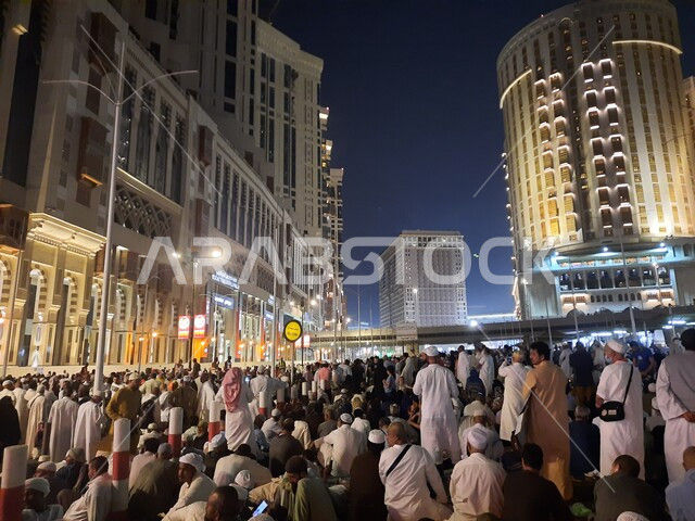 A group of visitors to the House of God sitting in the streets of Mecca, Saudi Arabia at night, streets and roads, pilgrims and Umrah pilgrims, towers and hotels in Mecca, Saudi landmarks, tourism in Saudi Arabia
