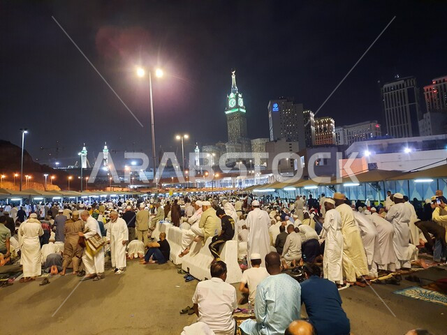 A group of visitors to the House of God sitting in the streets of Mecca, Saudi Arabia at night, streets and roads, pilgrims and Umrah pilgrims, clock tower, Saudi landmarks, tourism in Saudi Arabia