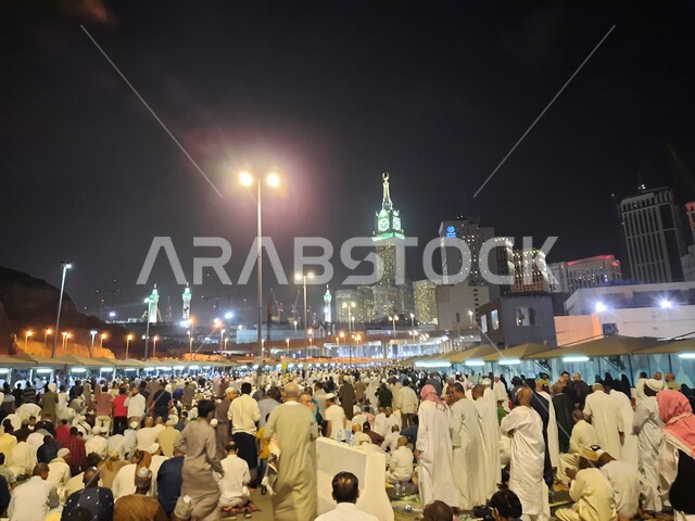 A group of visitors to the House of God sitting in the streets of Mecca, Saudi Arabia at night, streets and roads, pilgrims and Umrah pilgrims, clock tower, Saudi landmarks, tourism in Saudi Arabia
