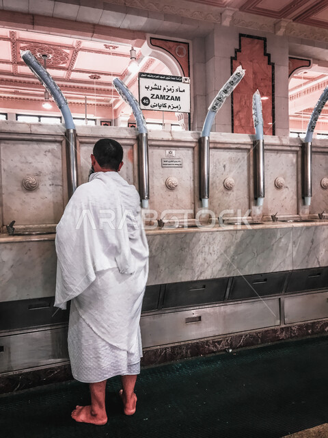 زاوية من الخلف لحاج يشرب من ماء زمزم ، ماء زمزم للشرب ، مياه زمزم في مكة المكرمة بالمملكة العربية السعودية