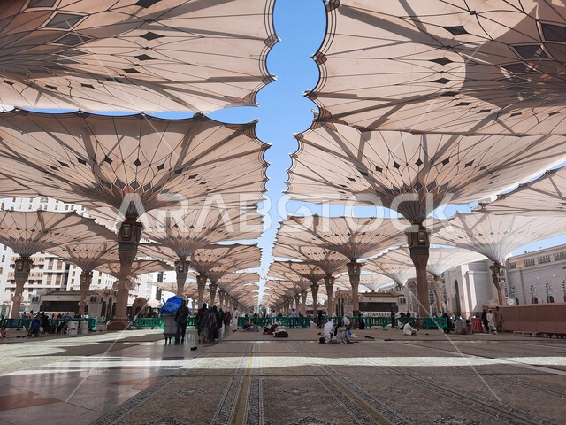 ساحة المسجد النبوي الشريف في المدينة المنورة بالمملكة العربية السعودية، العبادة والتقرب الى الله، الحرم النبوي الشريف، أماكن إسلامية مقدسة، المسلمون يمشون في المجمع الخارجي للمسجد النبوي في المدينة المنورة، المظلات الإلكترونية