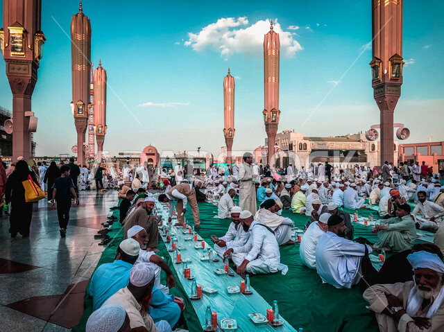 مجموعة من المسلمين يجلسون على مائدة الافطار الجماعي في ساحة المسجد النبوي الشريف في المدينة المنورة بالمملكة العربية السعودية، الحرم النبوي الشريف، مائدة الافطار، أماكن إسلامية مقدسة، المجمع الخارجي للمسجد النبوي الشريف، المعالم الدينية بالسعودي