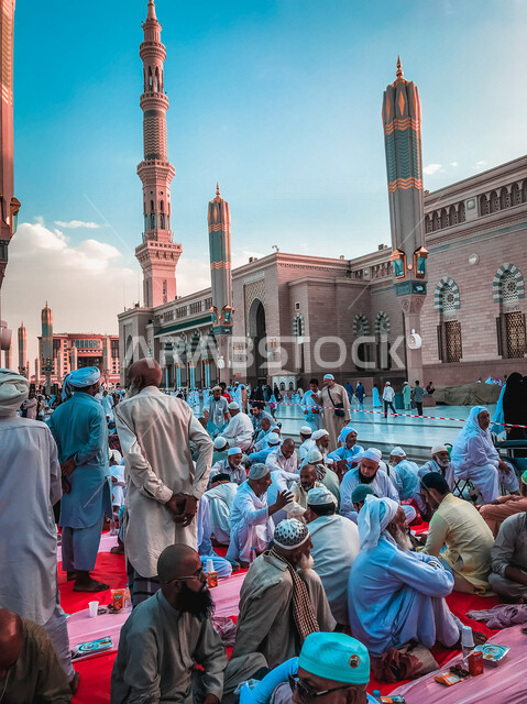 مجموعة من المسلمين يجلسون على مائدة الافطار الجماعي في ساحة المسجد النبوي الشريف في المدينة المنورة بالمملكة العربية السعودية، الحرم النبوي الشريف، مائدة الافطار، أماكن إسلامية مقدسة، المجمع الخارجي للمسجد النبوي الشريف، المعالم الدينية بالسعودي