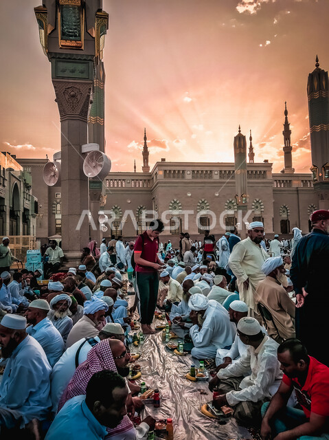 مجموعة من المسلمين يجلسون على مائدة الافطار الجماعي في ساحة المسجد النبوي الشريف في المدينة المنورة بالمملكة العربية السعودية، الحرم النبوي الشريف، مائدة الافطار، أماكن إسلامية مقدسة، المجمع الخارجي للمسجد النبوي الشريف، المعالم الدينية بالسعودي