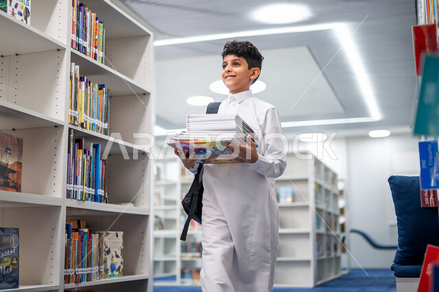 طالب عربي سعودي خليجي يحمل مجموعه من الكتب داخل المكتبة المدرسية، الاستمتاع بقراءة الكتب المدرسية، مفهوم التعليم والثقافه, مكتبة المدرسة، التعليم الذاتي, بيئه مدرسيه تعليميه متطوره, مدارس أكاديميه في المملكة العربية السعودية