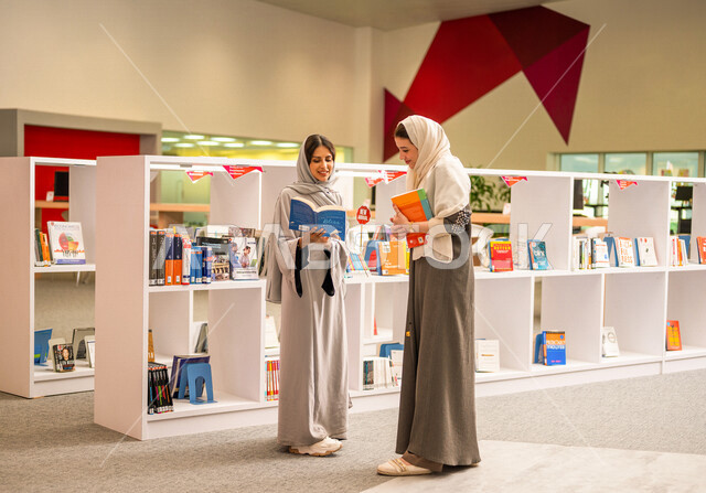 إمرأتان عربيتان سعوديتان خليجيتان في بيئة جامعيه تعليمية متطورة, طالبات جامعيات, قراءة الكتب في مكتبة الجامعه، التعليم الذاتي, مفهوم القراءه والثقافه، جودة التعليم, جامعات اكاديميه في المملكه العربيه السعوديه, برامج أكاديميه, كليات و جامعات متطوره