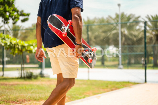 Angle from the back of a Saudi Arabian Gulf man, holding a skateboard in one of the recreational parks in Saudi Arabia, recreational tourist places, spending fun times, recreational activities, practicing skateboarding