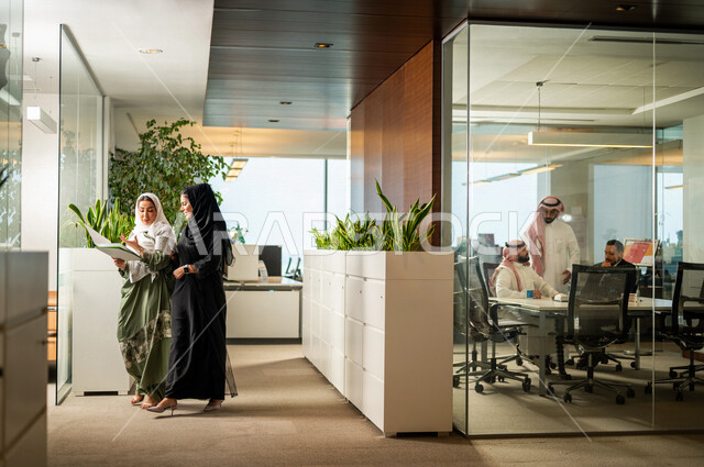  موظفتان عربيتان سعوديتان خليجيتان داخل مقر الشركة، ترتديان عبايات عصرية مميزة، أزياء محجبات، مهن و وظائف سعودية، شركة سعودية، سيدات أعمال، الحوارات والنقاشات، بيئة العمل، دردشة عمل، غرفة إجتماعات، متابعة ومناقشة الأعمال