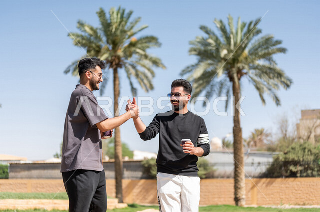 شابان عربيان خليجيان سعوديان يتقابلان في احد الحدائق العامة ويتصافحان بابتسامة، ممارسة رياضة المشي الهواء الطلق مع احتساء كوب من القهوة، التصافح بحرارة، تعارف وصداقات، السلام والترحيب، طريق ممشى في الحدائق والمنتزهات، نزهه في الهواء الطلق