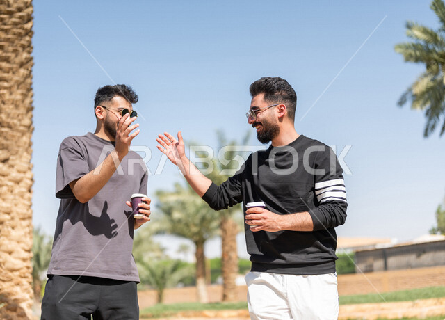 شابان عربيان خليجيان سعوديان يتقابلان في احد الحدائق العامة ويتصافحان بابتسامة، ممارسة رياضة المشي الهواء الطلق مع احتساء كوب من القهوة، التصافح بحرارة، تعارف وصداقات، السلام والترحيب، طريق ممشى في الحدائق والمنتزهات، نزهه في الهواء الطلق