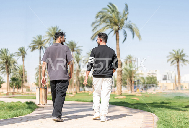 صورة من الخلف لصديقان عربيان خليجيان سعوديان يمارسان الرياضة الصباحية، ممارسة رياضة المشي، قضاء اوقات ممتعة في الحدائق العامة، دردشة ومحادثات، نشاط بدني، طريق ممشى في الحدائق والمنتزهات، ممارسة التمارين الرياضية، نزهه في الهواء الطلق