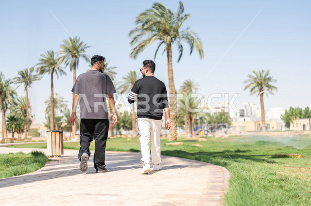 صورة من الخلف لصديقان عربيان خليجيان سعوديان يمارسان الرياضة الصباحية، ممارسة رياضة المشي، قضاء اوقات ممتعة في الحدائق العامة، دردشة ومحادثات، نشاط بدني، طريق ممشى في الحدائق والمنتزهات، ممارسة التمارين الرياضية، نزهه في الهواء الطلق