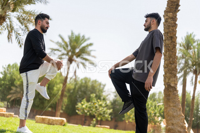 Two Saudi Arabian Gulf youths practicing stretching exercises, stretching the muscles of the body, practicing sports activities, sports activities and exercises, sports and physical activity, fitness exercises, healthy lifestyle, fitness and agility