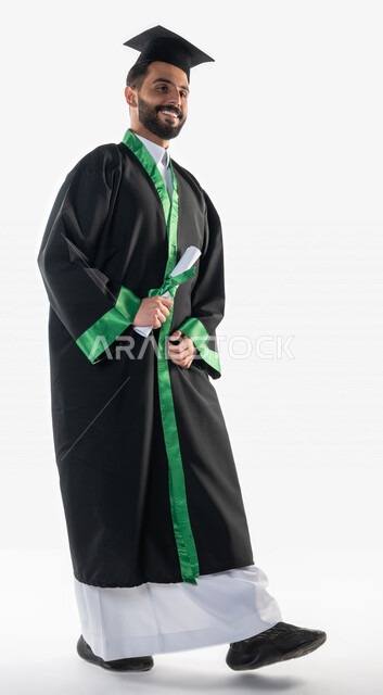 بورتريه لطالب عربي سعودي خليجي يرتدي العباءه وقبعة التخرج، يمسك بيده شهادة التفوق والنجاح, التحرك والمشي ايماءات تدل على الشعور بالفخر والسعاده, خريج جامعي، حفل تخرج، اللباس الاكاديمي، صوره للجسم بالطول الكامل, التعليم في السعوديه, خلفية بيضاء