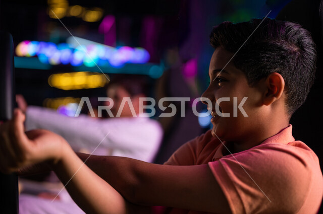 Close-up of a Saudi Arabian Gulf boy in the electronic game store, racing car game, sitting behind the wheel of the car (controller), electronic video games, gaming technology, entertainment activities, spending leisure time playing video games with frien