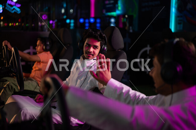 شابان مراهقان عربيان خليجيان سعوديان يتصافحان في متجر الألعاب الإلكترونية، لعبة سيارات سباق، الجلوس خلف عجلة مقود السيارة (يد التحكم)، تحديات ومنافسات،  أنشطة ترفيهية، قضاء وقت الفراغ بألعاب الفيديو مع الأصدقاء، الإستعداد لبدء التحدي، تصافح اللاعبين
