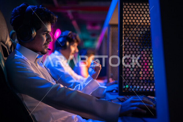 Young Arab Gulf Saudi teens in an electronic game store, wearing a headset and playing electronic video games, gestures indicating integration and interaction, recreational activities, computer entertainment, spending leisure time playing video games with