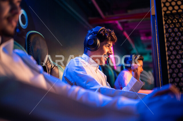 شباب عرب مراهقين خليجيين سعوديين في متجر الألعاب الإلكترونية، يرتديان سماعة الرأس ويلعبان ألعاب الفيديو الإلكترونية، إيماءات تدل على الإندماج والتفاعل، أنشطة ترفيهية، ألعاب الكمبيوتر الترفيهية، قضاء وقت الفراغ بألعاب الفيديو مع الأصدقاء، اللعب الجماعي