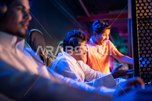 Young Arab Gulf Saudi teens in an electronic game store, wearing a headset and playing electronic video games, gestures indicating integration and interaction, recreational activities, computer entertainment, spending leisure time playing video games with