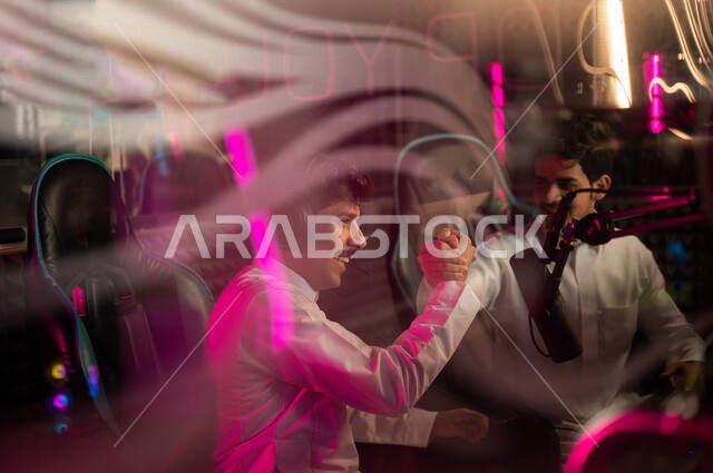 شابان مراهقان عربيان خليجيان سعوديان يتصافحان في متجر الألعاب الإلكترونية، شاب سعودي يرتدي سماعة الرأس، جيمر سعودي محترف بألعاب الفيديو الإلكترونية، منصة البث المباشر في عالم ألعاب الفيديو، ألعاب الفيديو الإلكترونية، تكنولوجيا الألعاب