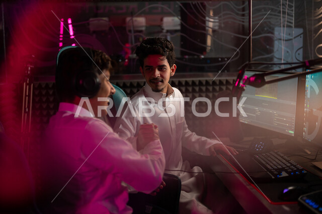 شابان مراهقان عربيان خليجيان سعوديان يتصافحان في متجر الألعاب الإلكترونية، شاب سعودي يرتدي سماعة الرأس، جيمر سعودي محترف بألعاب الفيديو الإلكترونية، منصة البث المباشر في عالم ألعاب الفيديو، ألعاب الفيديو الإلكترونية، تكنولوجيا الألعاب