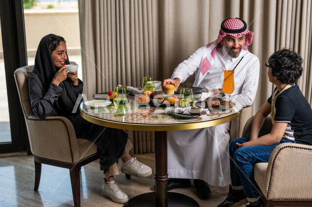 عائلة عربية خليجية سعودية تجلس في المطعم، مائدة طعام مليئة بأصناف متنوعة من المأكولات والمشروبات الشهية، نقاشات وحوارات عائلية، تعابير تدل على السعادة، قضاء أوقات عائلية ممتعة، سفرة طعام، اجواء عائلية سعيدة، مطاعم وكافيهات راقية في السعودية