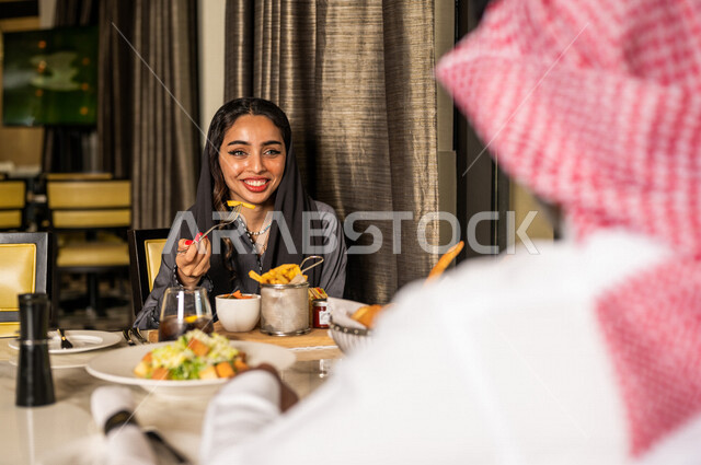زوجان عربيان سعوديان خليجيان يجلسان في مطعم، مائدة طعام مليئة بأصناف متنوعة من المأكولات والمشروبات الشهية، نقاشات وحوارات عائلية، تعابير تدل على السعادة، قضاء أوقات عائلية ممتعة، سفرة طعام، اجواء عائلية سعيدة، مطاعم وكافيهات راقية في السعودية