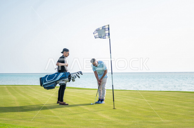 رجلان عربيان خليجيان سعوديان يرتديان الزي الرياضي، ممارسة لعبة الغولف على مساحات واسعة خضراء، أنشطة رياضية بالسعودية، لعبة الجولف، رياضات الألعاب الأولمبية الصيفية، أنشطة ترفيهية، ملعب الجولف، الإستمتاع باللعب، تحديد وتصويب الهدف