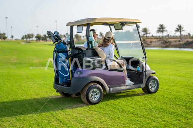 رجل وإمرأة عربيان خليجيان سعوديان داخل سيارة كهربائية مختصة بنقل الركاب، لعبة الغولف ( الجولف ) ، أنشطة رياضية بالسعودية، رياضات الألعاب الأولمبية الصيفية، أنشطة ترفيهية، ملعب الجولف، سيارة كهربائية، نادي الجولف، عربة الجولف
