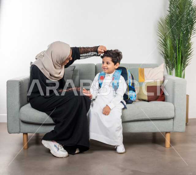 أم عربية خليجية سعودية تقوم بتجهيز ابنها للذهاب الى المدرسة، ارتداء الزي المدرسي، الاستعداد للذهاب الى المدرسة، حقيبة الظهر المدرسية، مفهوم الأمومة والطفولة، الاستعداد للفصل الدراسي الجديد، سنة دراسية جديدة، العودة الى المدرسة