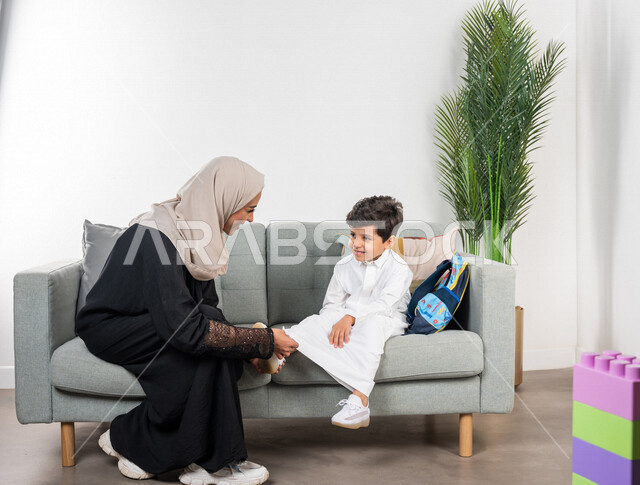 أم عربية خليجية سعودية تقوم بتجهيز ابنها للذهاب الى المدرسة، ارتداء الزي المدرسي، الاستعداد للذهاب الى المدرسة، حقيبة الظهر المدرسية، مفهوم الأمومة والطفولة، الاستعداد للفصل الدراسي الجديد، سنة دراسية جديدة، العودة الى المدرسة