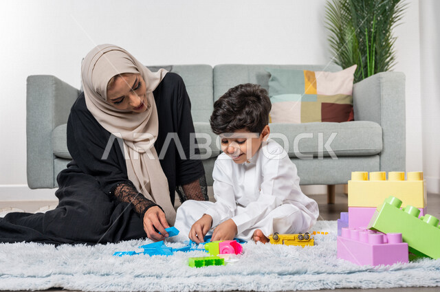 A veiled Saudi Gulf Arab mother plays with her child, practicing recreational activities, happy facial gestures, the concept of motherhood and childhood, recreational activities for the child, caring for children, developing child skills, caring and suppo
